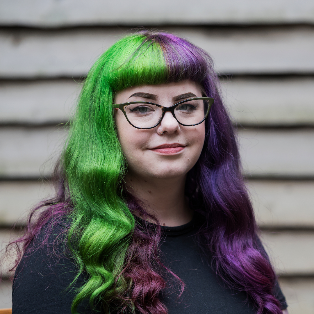 Megan has long hair that is green one side and purple the other, she wears green cat eye glasses