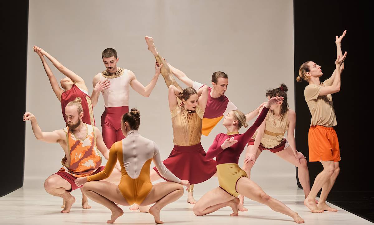 dancers in red and orange costumes posing together centre stage