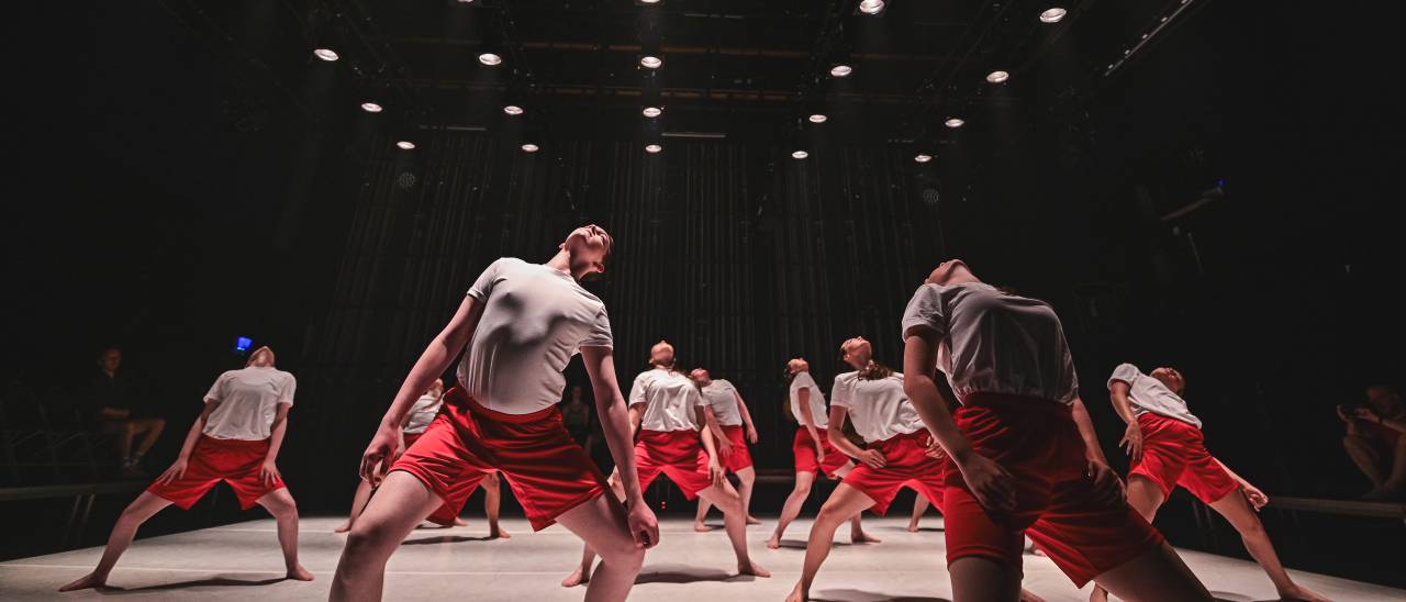 young dancers in red shorts and white t-shirts leaning backwards
