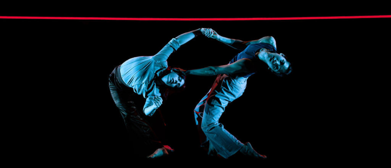 two dancers under blue light leaning under a red neon strip