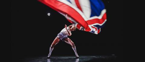 Male dancer in heels and stockings waving a British flag above his head
