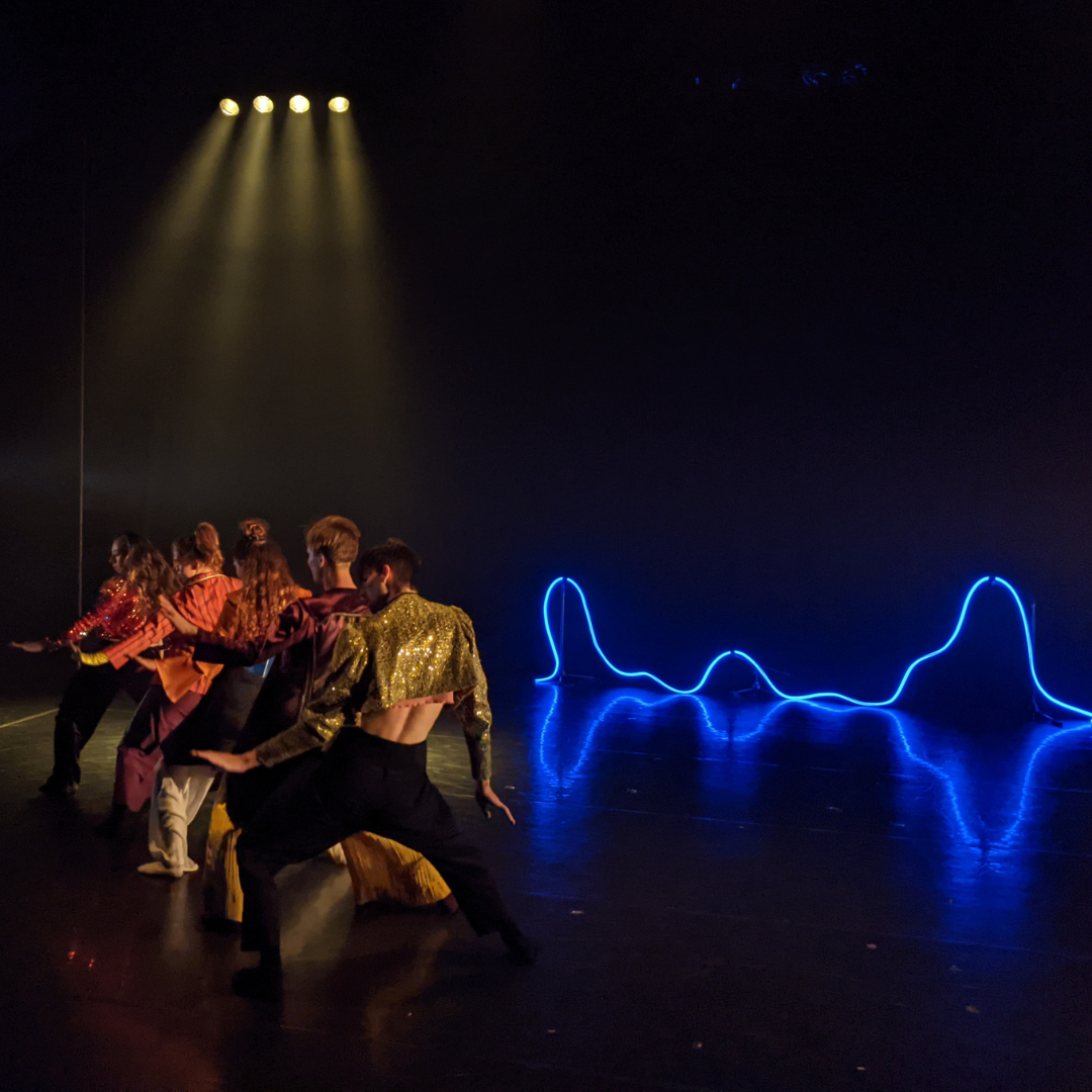 dancers in glittering costumes in front of a blue neon light