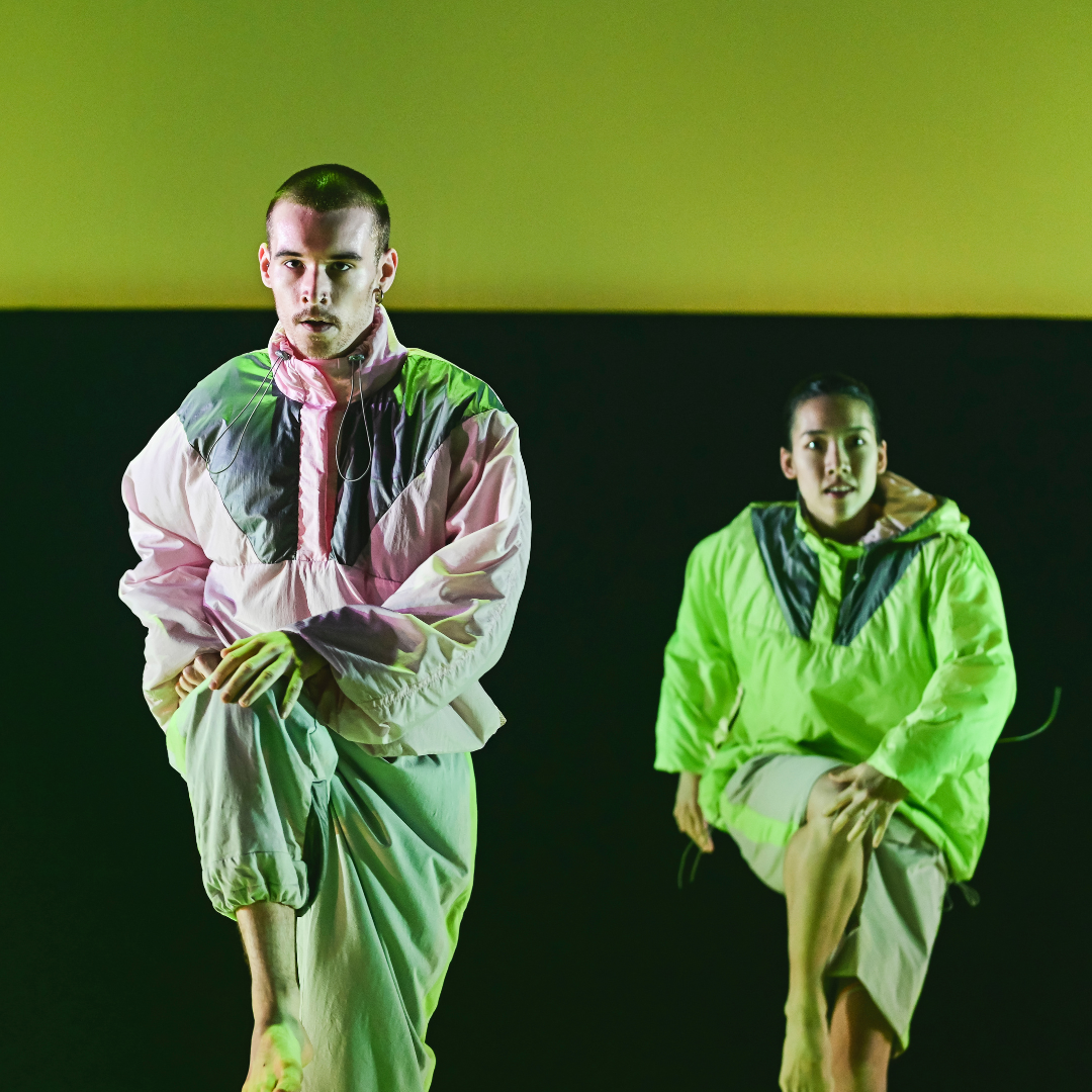 two dancers in neon costumes under yellow light
