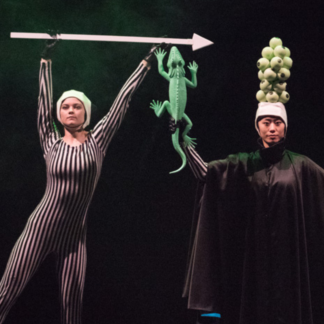 a dancer holds a large lizard prop