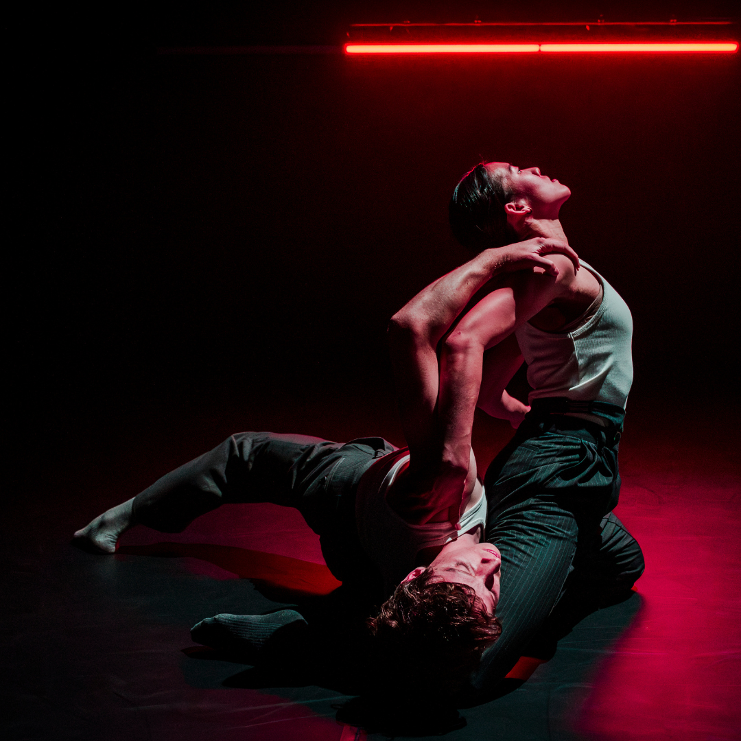 two dancers in pinstripe trousers under a red light