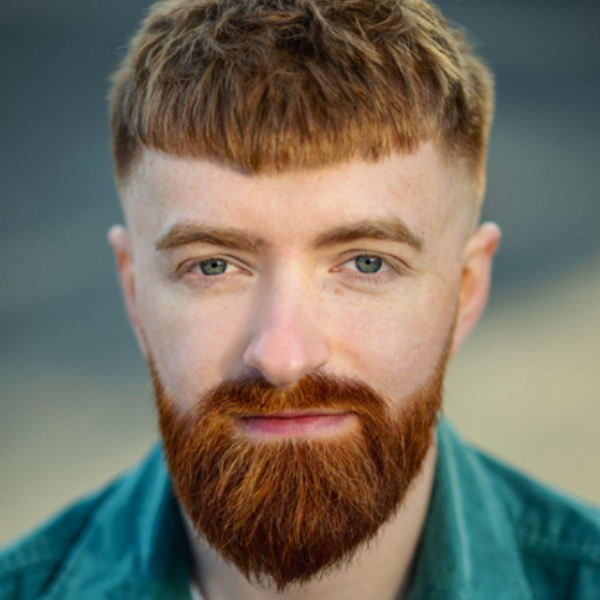 Kyle has short ginger hair and a neat but full ginger beard and kind eyes