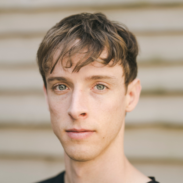 Headshot of dancer Sam, he wears a black t-shirt and has short blonde hair with a longer fringe