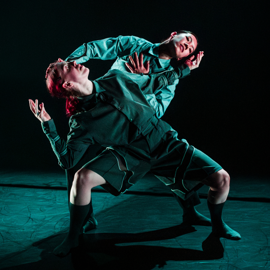 two dancers in deconstructed suits leaing away from one another whilst reaching for them