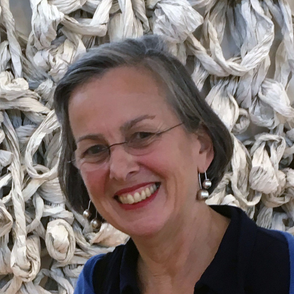 Cecile smiles infront of her own sculpture, she has a grey bob, glasses and red lipstick with a wide smile of perfect teeth 