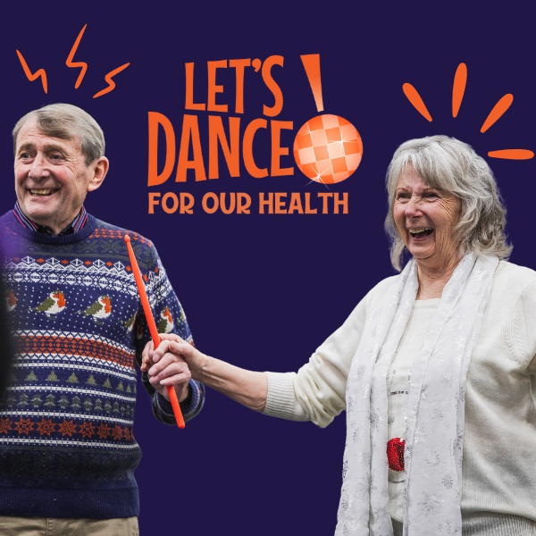 two participants at dance for parkinsons grinning madly whilst holding drumsticks and wearing christmas jumpers