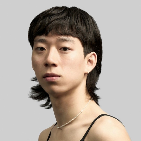 Jason has a sleek mullet style hair cut and wears a delicate necklace 