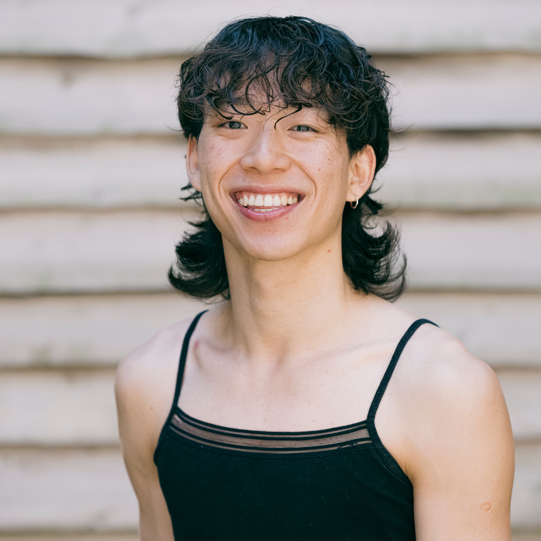 Jason has a sleek mullet style hair cut and wears a a black strap top