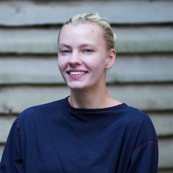 Masie smiles widely, wearing blonde hair pulled back into a bun and a navy t-shirt