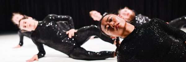 dancers in sparkly sequin costumes leaning over on a white floor 