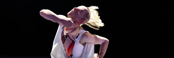 a dancer under dramatic lighting in a mask that compeletely covers his face, throwing his head backwards, fake hair attached to the mask flying upwards 