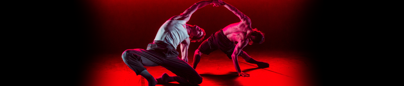 two dancers stretching out and upwards under a strong red light