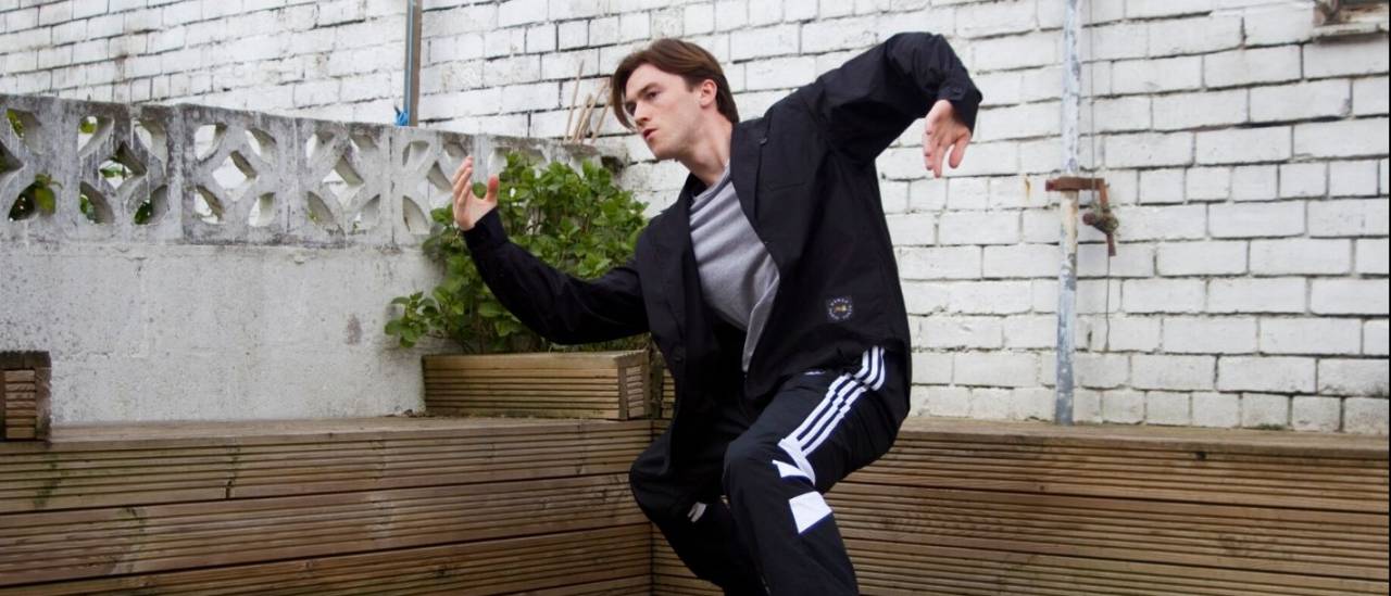 Mat in a garden wearing a black tracksuit arms stretched out in front and behind him