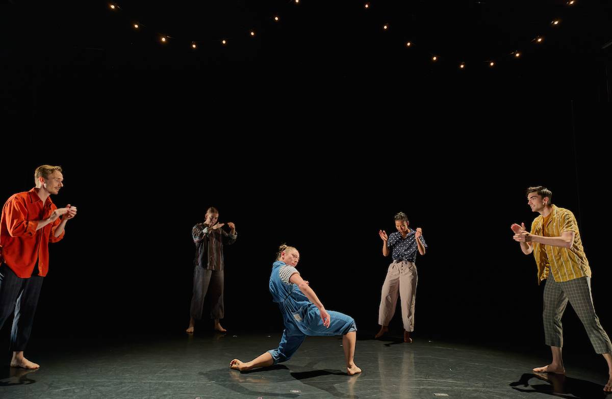 four dancers clapping in a circle with one in the centre leaning backwards 