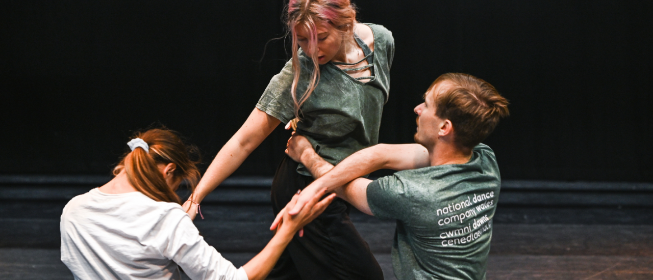three dancers moving together whilst touching hands 
