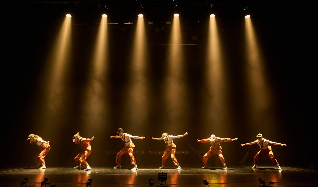 6 dancers in a row under a spotlight