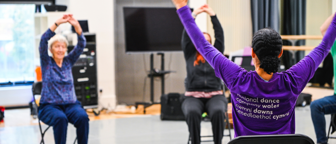 dance leader with arms in air and parkinson's participant facing her, copying and smiling