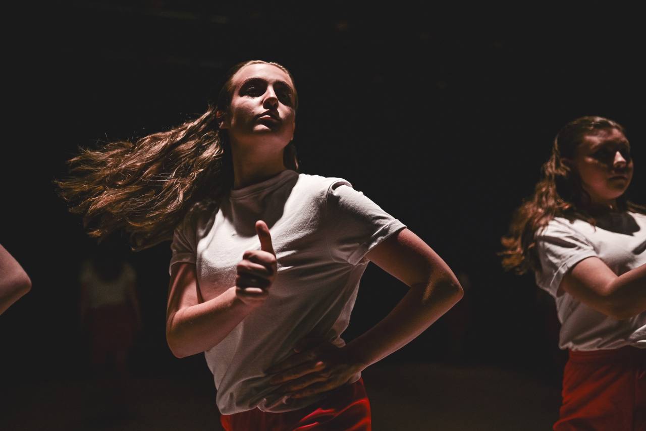 a young dancer turns, hair flying out behind her, doing a thumbs up with one hand