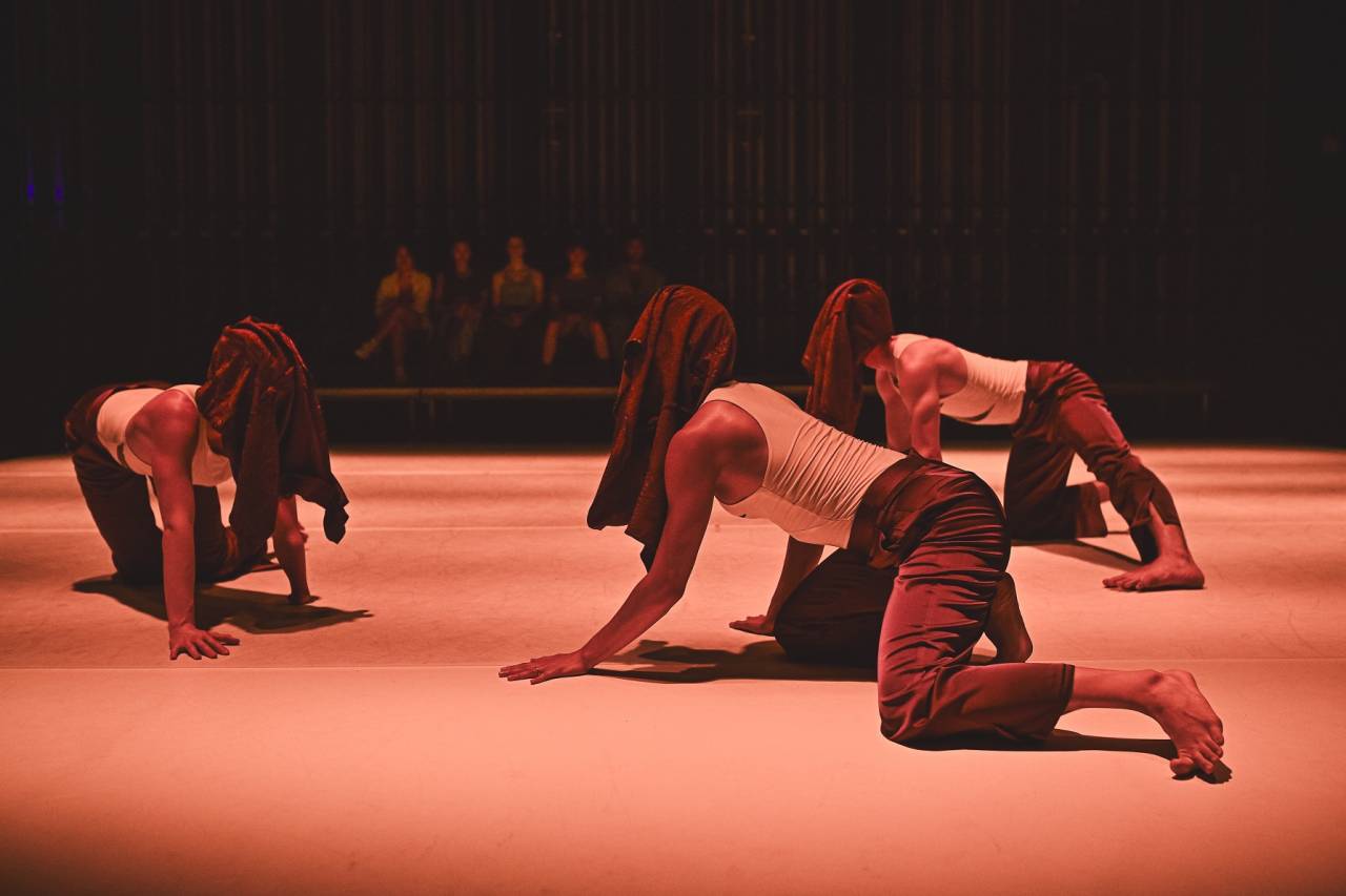 three dancers crawl around with their shirts over their heads as if masks
