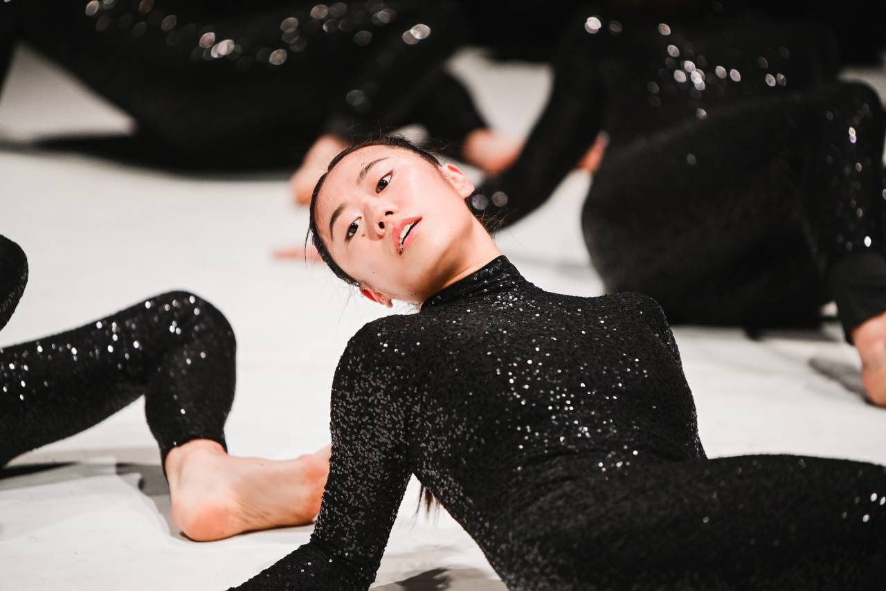 Jill leans back, lying on the floor in sparkly black costume with a serene look on her face