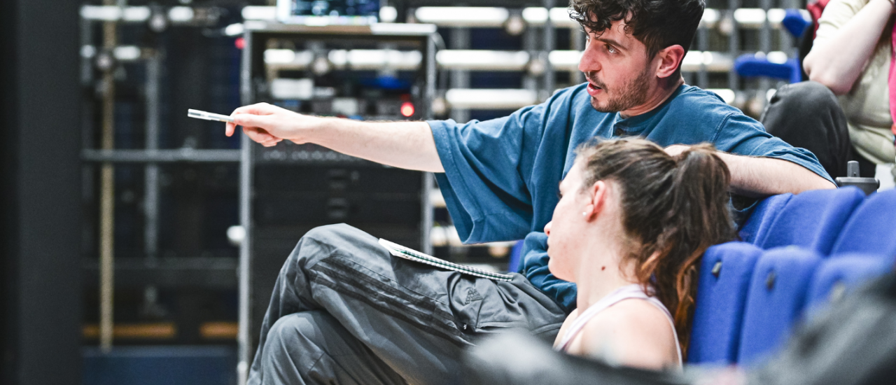 a choreographer pointing at the stage with a pen and talking to the person sat beside him