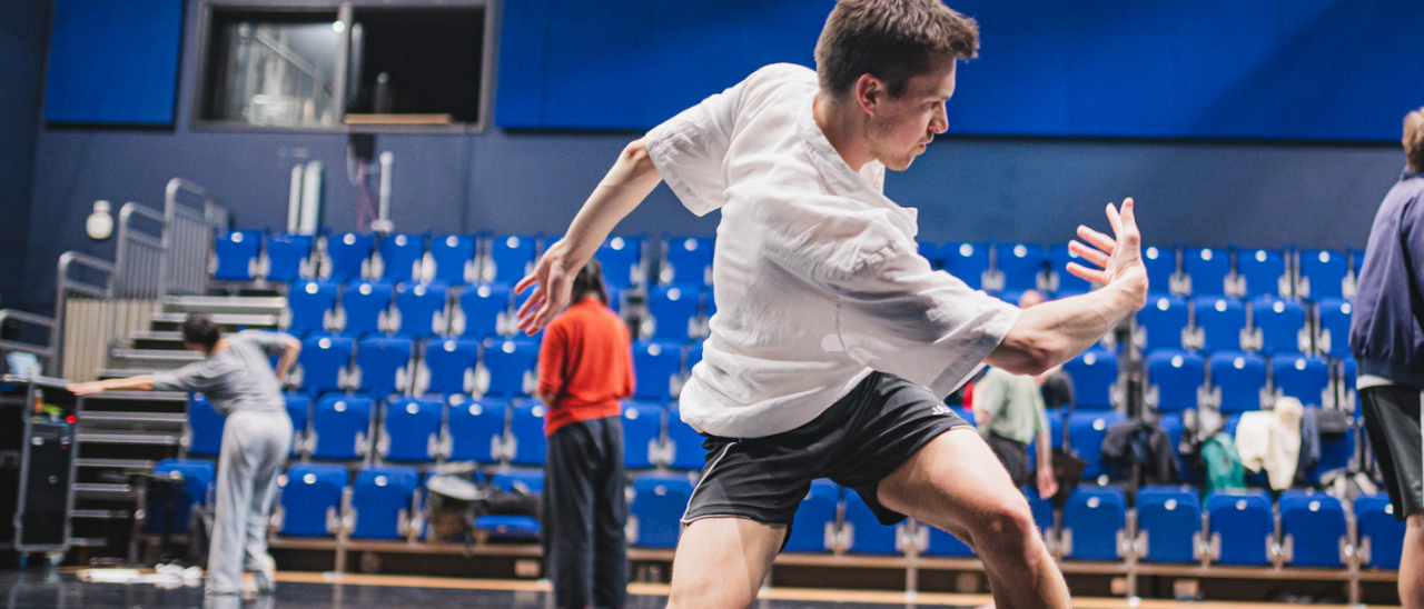 photo taken from back of studio facing seating, a dancer in foreground twists dynamically