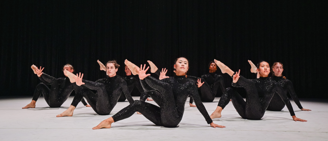 dancers in sequin body suits against a sequin curtain, sitting on the floor with a leg up