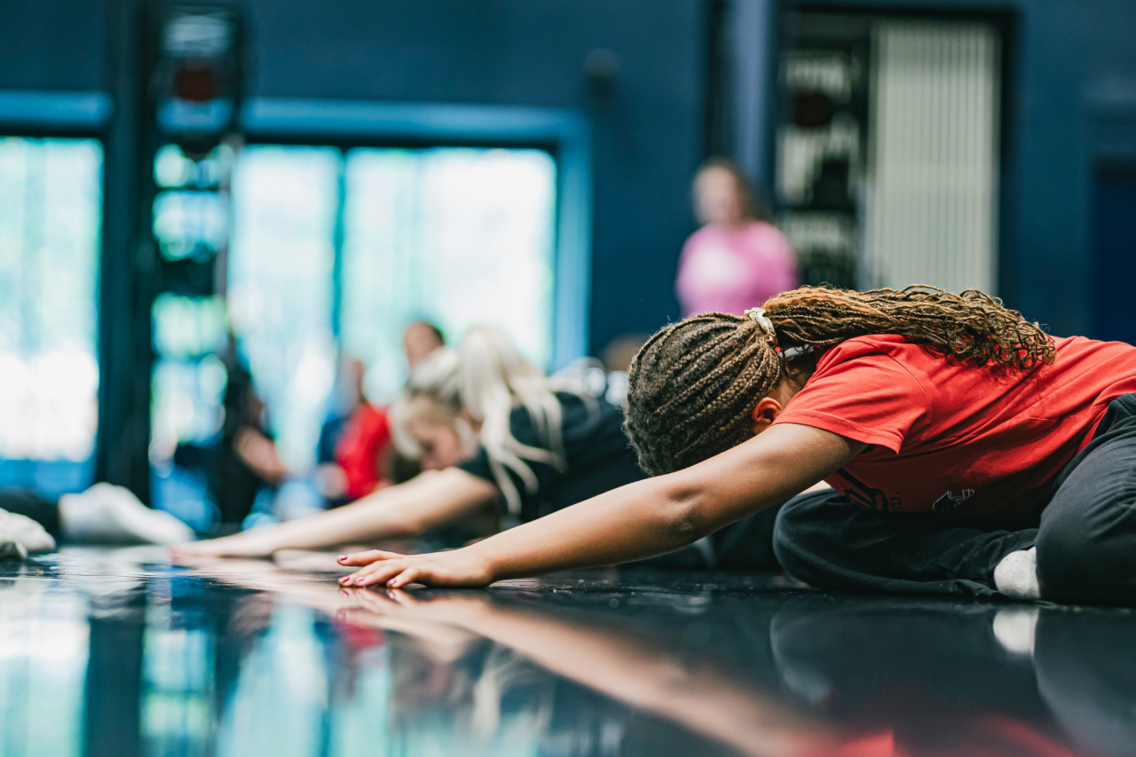 rehearsal, two young dancers kneel on the floor, heads bowed forward, arms stretching across the floor