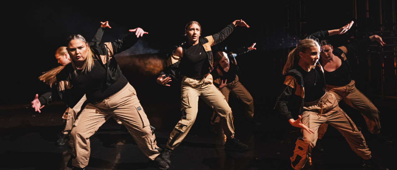 dancers in tan cargo trousers and black tops, arms out in a strong pose