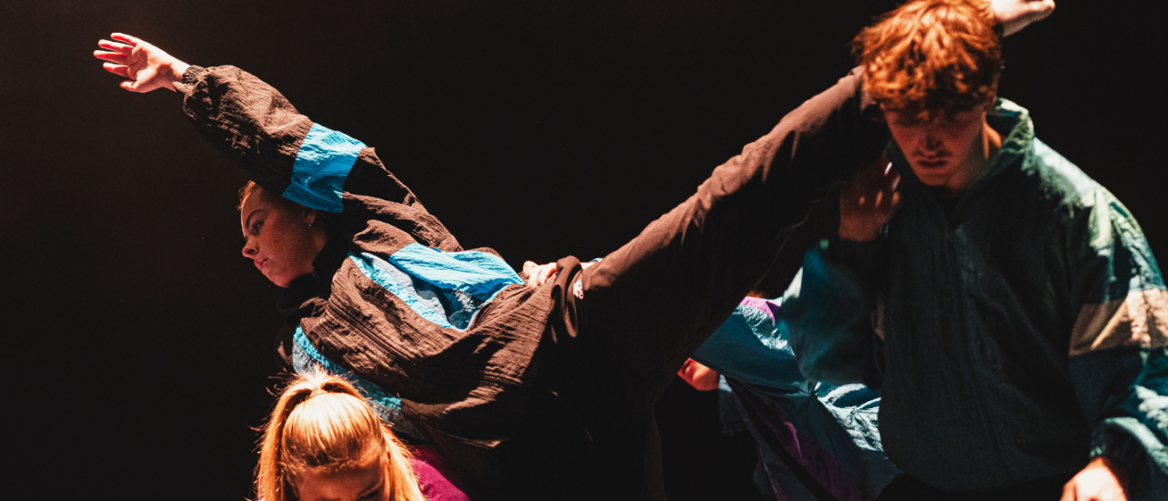 dancers stretching a leg over another one dressed in jewel tone tracksuits