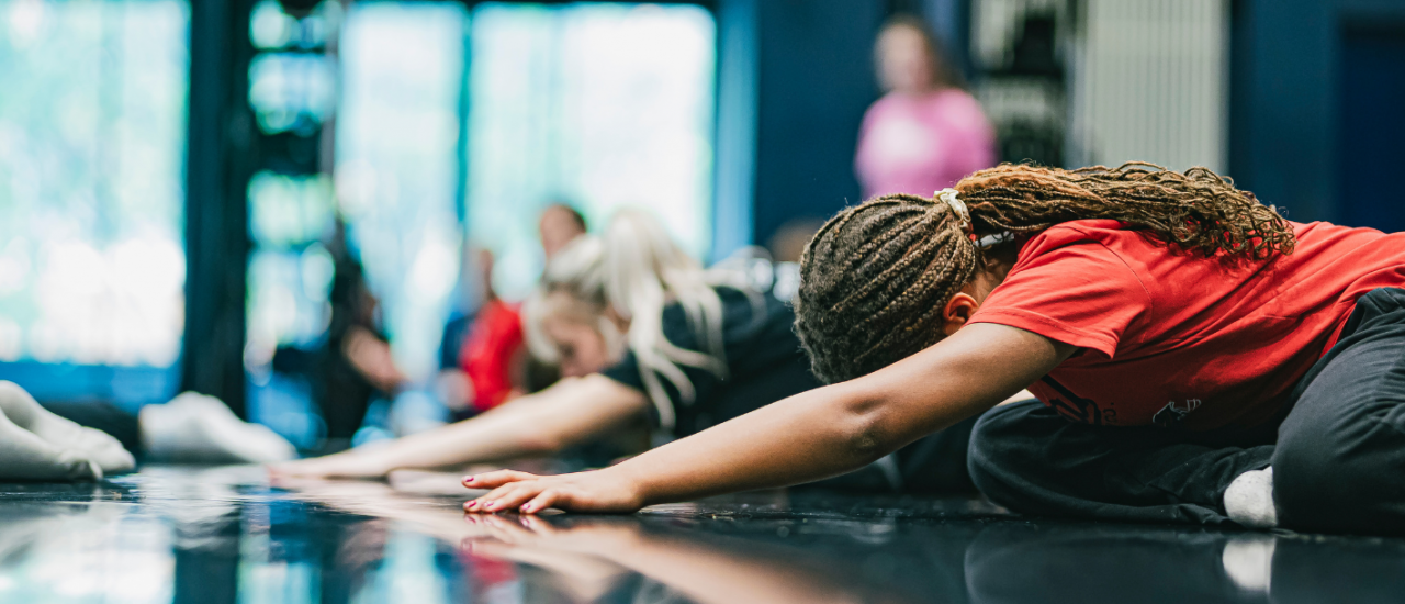 young dancers kneeling down and stretching their arms out infront of them