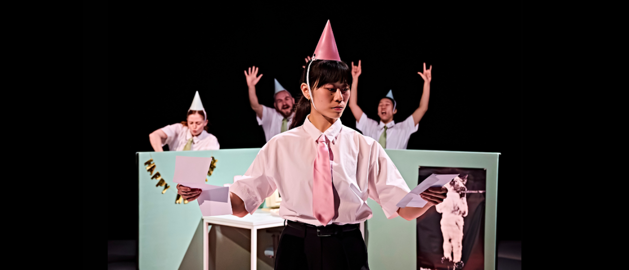 a dancer dressed in shirt and pink tie, and pink party hat looking at two documents, other dancers are having a party happily behind her