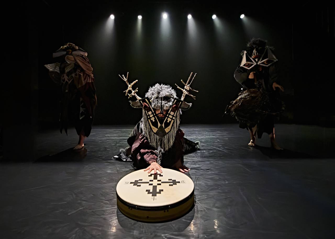 dancers in folk style circle, arms outstretched towards one another 