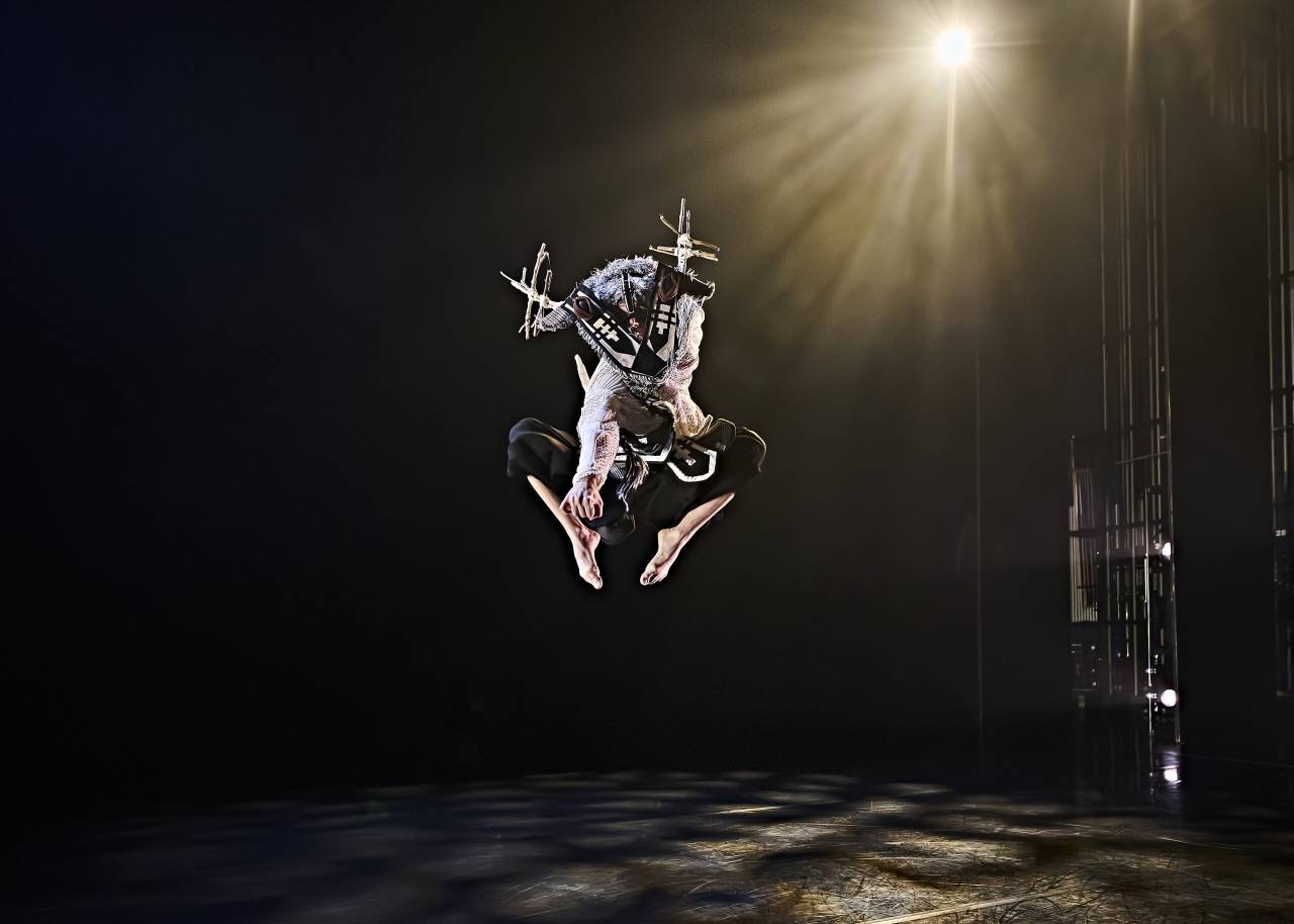 a dancer in a stag mask leaps high into the air 