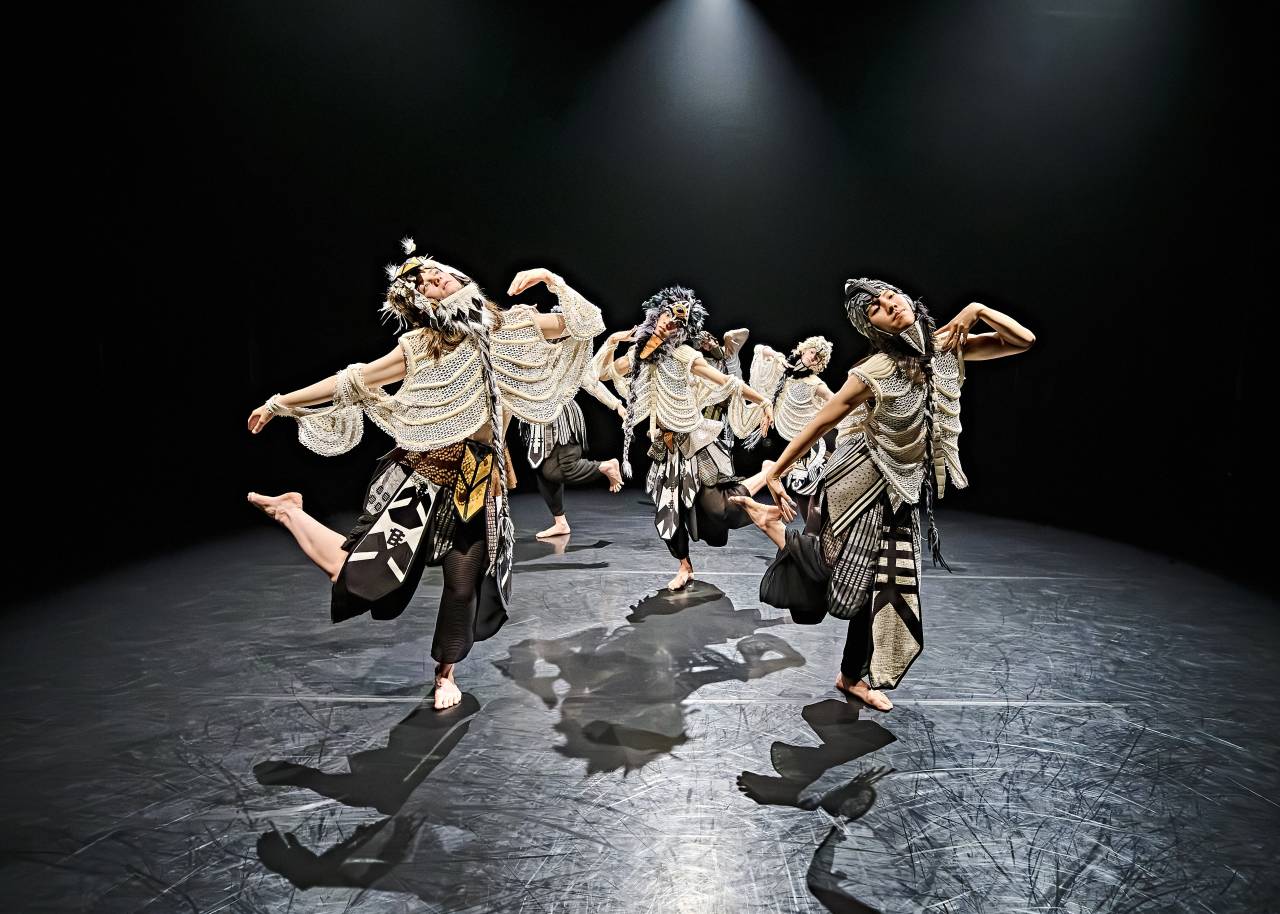 dancers in tops that look like rib cages dance in formation, four in a square and one in teh middle, their elbos and knees are bent outwards and heads thrown back, mid dance
