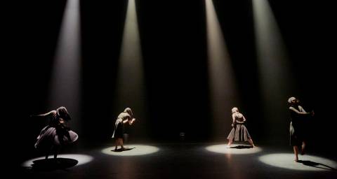 4 dancers each under a spotlight dressed in black
