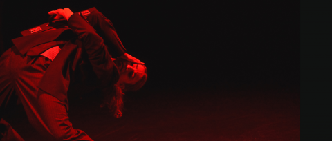 a dancer dressed in a suit holds a breifcase open in front of their face under a red light