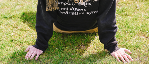 dancer in a ndcwales hoodies leans back on sunlit grass