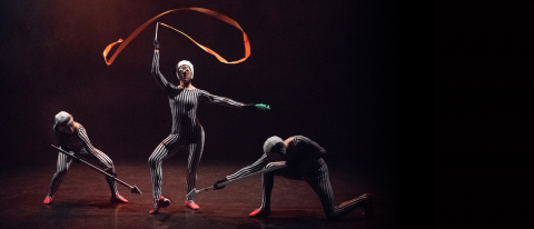 dancers in striped costumes and red ballet shoes holding arrows and waving ribbons whilst wearing funny glasses with fake eyeballs