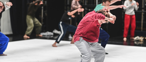 dancers take class together on a white dance floor wearing casual athletic clothes