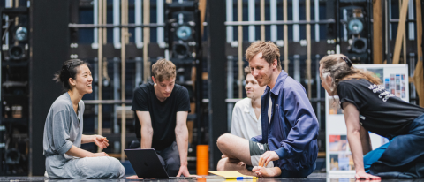 dancers in the studio gathered around a laptop, learning and laughing