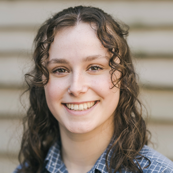 Charlotte has curly brown hair, a blue shirt and wide smile