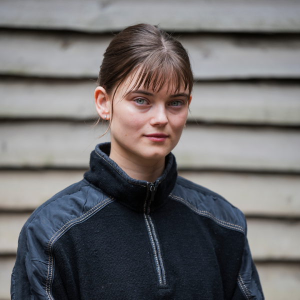 Riz has shoulder length brown hair with a fringe and wears fleece top